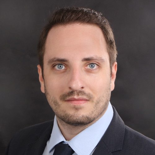 Kevin Müller Mann mit kurzem Haar, blauen Augen und Anzug vor einem dunklen Hintergrund.